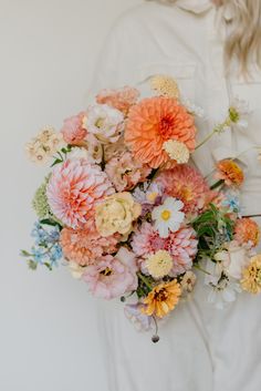 a woman holding a bouquet of flowers in her hands and wearing a white shirt behind her