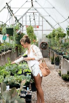 a woman is looking at plants in a greenhouse