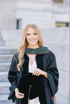 a woman wearing a graduation gown and holding a black hat in front of some steps