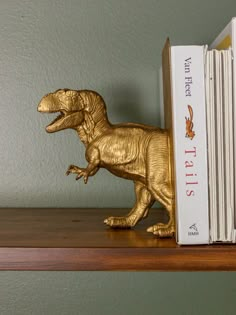 a gold dinosaur figurine sitting on top of a book shelf next to two books