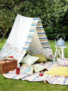 a teepee is set up in the grass with pillows and blankets on top of it