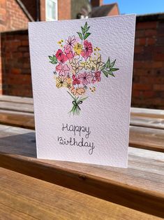 a happy birthday card with flowers on it sitting on a bench outside in front of a brick building