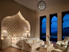 a bedroom with white furniture and large windows overlooking the ocean at night, is pictured in this image