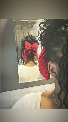 a woman with curly hair wearing a red knitted bow tie in front of a mirror