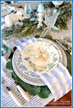 the table is set with blue and white plates, silverware, and greenery