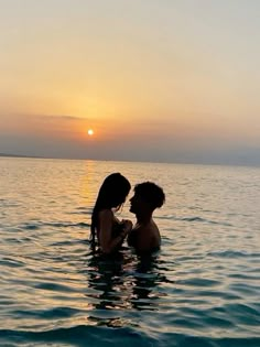 two people in the water at sunset with one holding the other's face to their chest