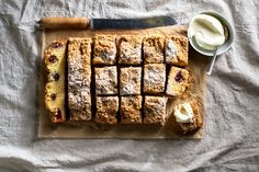 a cutting board topped with slices of fruit cake next to a bowl of whipped cream