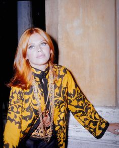 a woman with red hair wearing a black and yellow shirt standing in front of a pillar