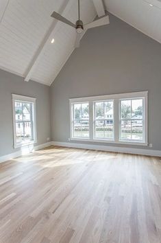 an empty room with two windows and hard wood flooring