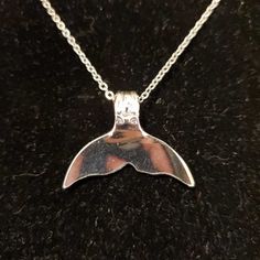 a silver necklace with a large shark tail on it's back end, sitting on a black surface