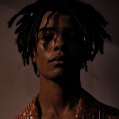 a man with dreadlocks standing in front of a white wall wearing a shirt and tie