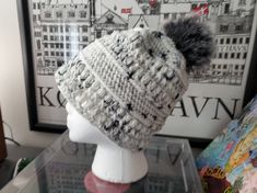 a white knitted hat with grey pom - poms on top of a mannequin head