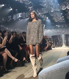 a model walks down the runway in a sequin - embellished dress and knee high boots