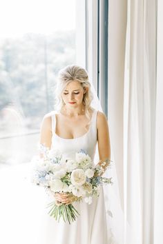 a woman in a white dress holding a bouquet of flowers and looking out the window