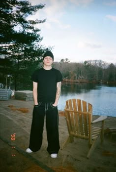 a man standing next to a wooden chair in front of a body of water on a sunny day