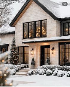 a white house with christmas lights on the windows and trees in snow covered front yard