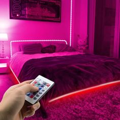 a person holding a remote control in front of a bed with pink lights on it