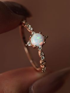 a woman's hand holding an opal and diamond ring