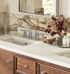 a bathroom sink sitting under a mirror next to a counter top with flowers in it