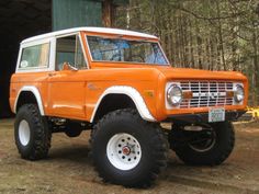 an orange and white truck parked in front of a building with large tires on it