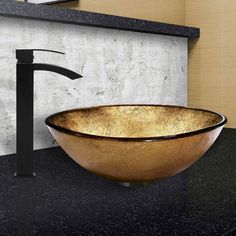 a bathroom sink with a black faucet and gold glass bowl on the counter