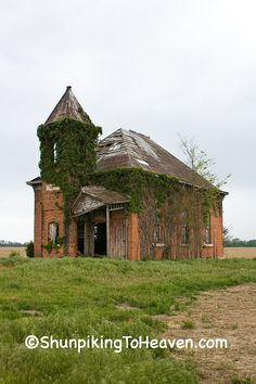 an old brick building with ivy growing on it's roof in the middle of a field