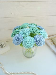 a vase filled with blue and green flowers on top of a table next to a book