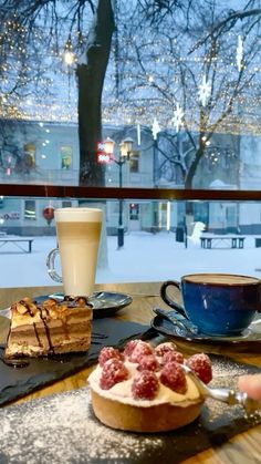 desserts and coffee sit on a table in front of a window with snowy trees