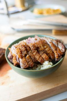 a green bowl filled with meat and rice on top of a wooden cutting board next to other food items