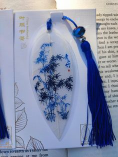 two bookmarks with blue tassels and flowers on them, one is hanging from a string