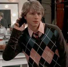 a young man is talking on his cell phone in front of a mirror while wearing a sweater and tie