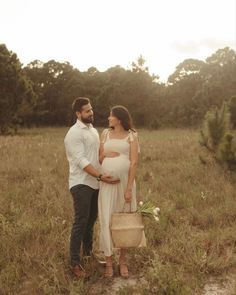 a pregnant couple standing in the middle of a field