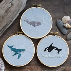 three embroidery hoops with whale images on them and seashells in the background