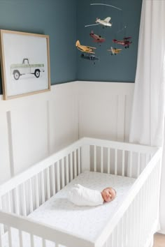 a baby in a white crib with toy airplanes hanging from the wall above it