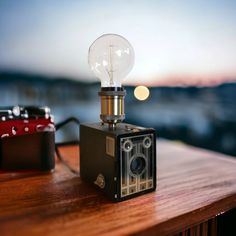 an old fashioned camera sitting on top of a wooden table next to a light bulb