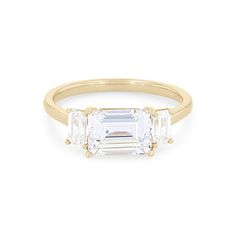 an emerald and diamond three stone ring in yellow gold, set on a white background