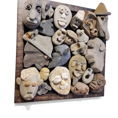 a group of rocks with faces on them are arranged in a wooden frame and displayed against a white wall