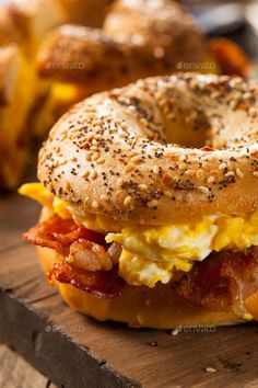 a bagel sandwich with bacon, egg and cheese on it sitting on a cutting board