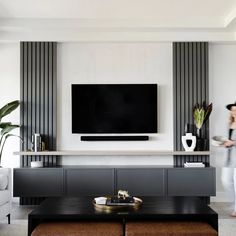 a woman standing in front of a flat screen tv mounted on a wall above a coffee table