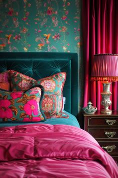 a bed with pink and green pillows on top of it next to a red lamp