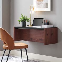 a desk with a laptop on it next to a chair and potted plant in the corner