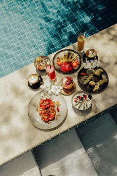 a table that has some food on it next to a swimming pool with water in the background