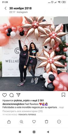 two women standing next to each other in front of balloons and flowers on the wall