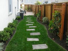 a garden with grass and stepping stones in the middle, along side a fenced yard