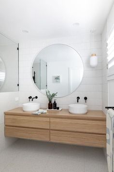 a bathroom with two sinks and a large round mirror above the sink, in front of a white tiled wall