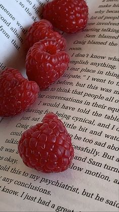 three raspberries are laying on top of an open book and one is red