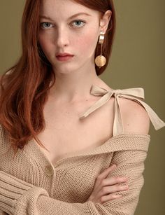 a woman with red hair and blue eyes wearing a beige sweater is posing for the camera