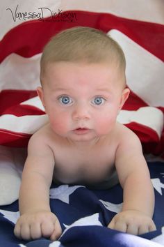 a baby with blue eyes laying on top of an american flag blanket and looking at the camera