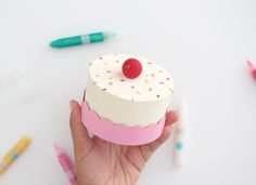 a hand holding a small cupcake decorated with sprinkles and a cherry