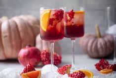 two glasses filled with red wine and garnished with oranges, raspberries and pomegranate